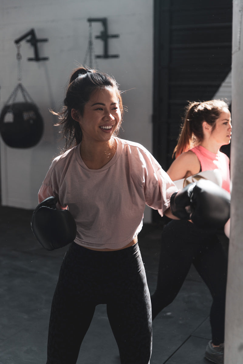 Woman in boxing class smiles and lightly punches the punching bag