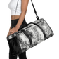 Woman in white top and black leggings carries New City Adventure duffle bag in black and white speckle pattern front view