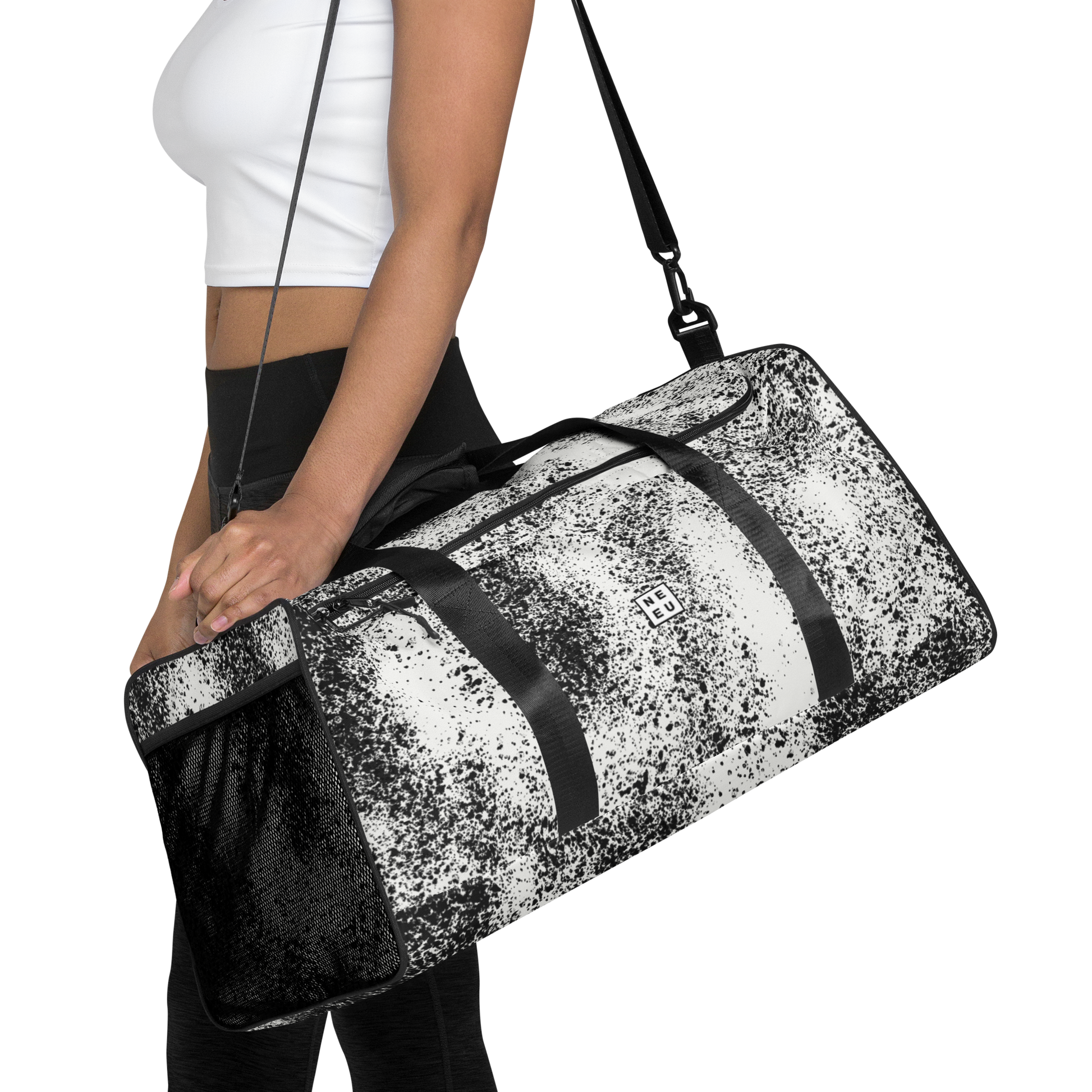 Woman in white top and black leggings carries New City Adventure duffle bag in black and white speckle pattern front view