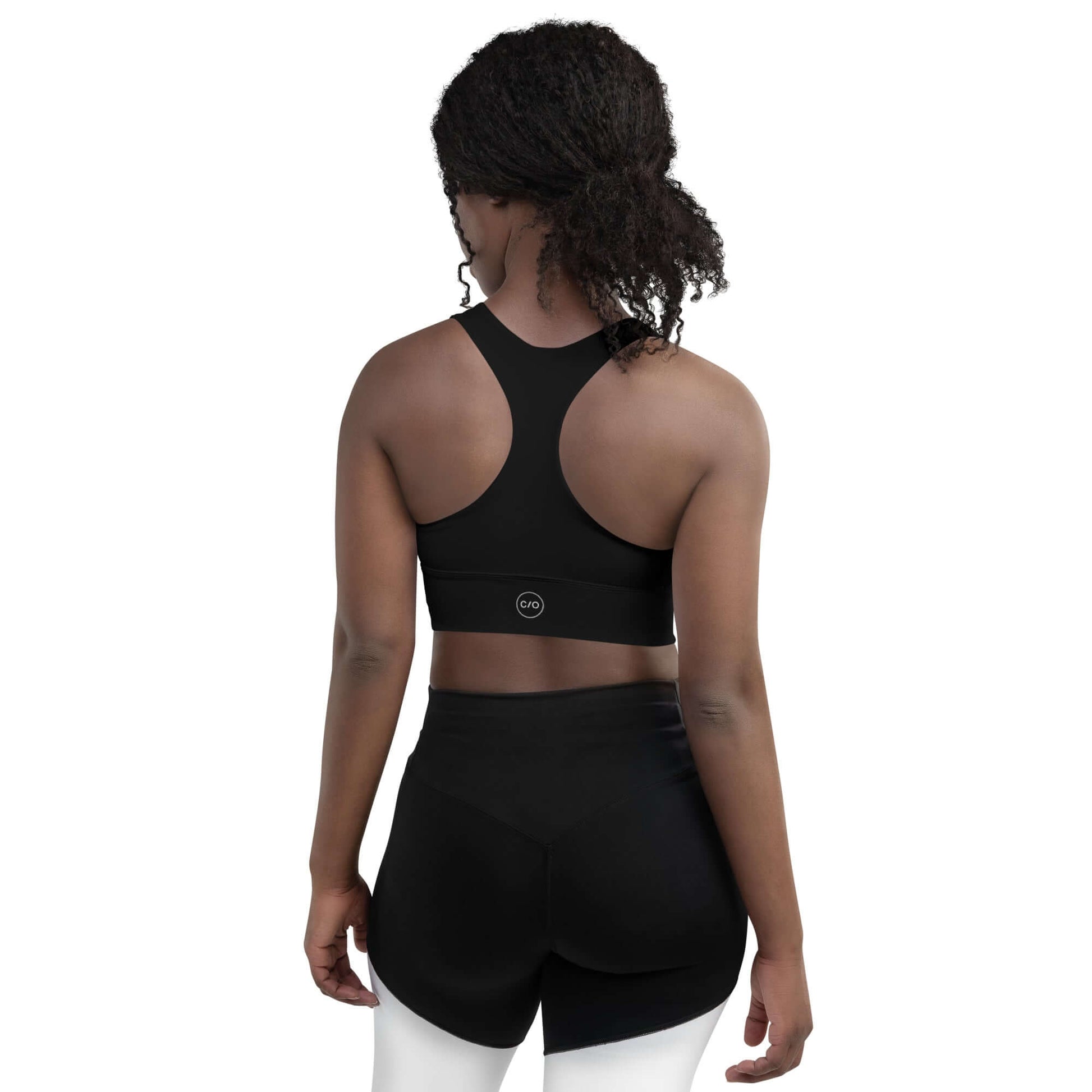 Woman wears Neue Supply Co. Longline Sports Bra in Black. Back view of model on white background.