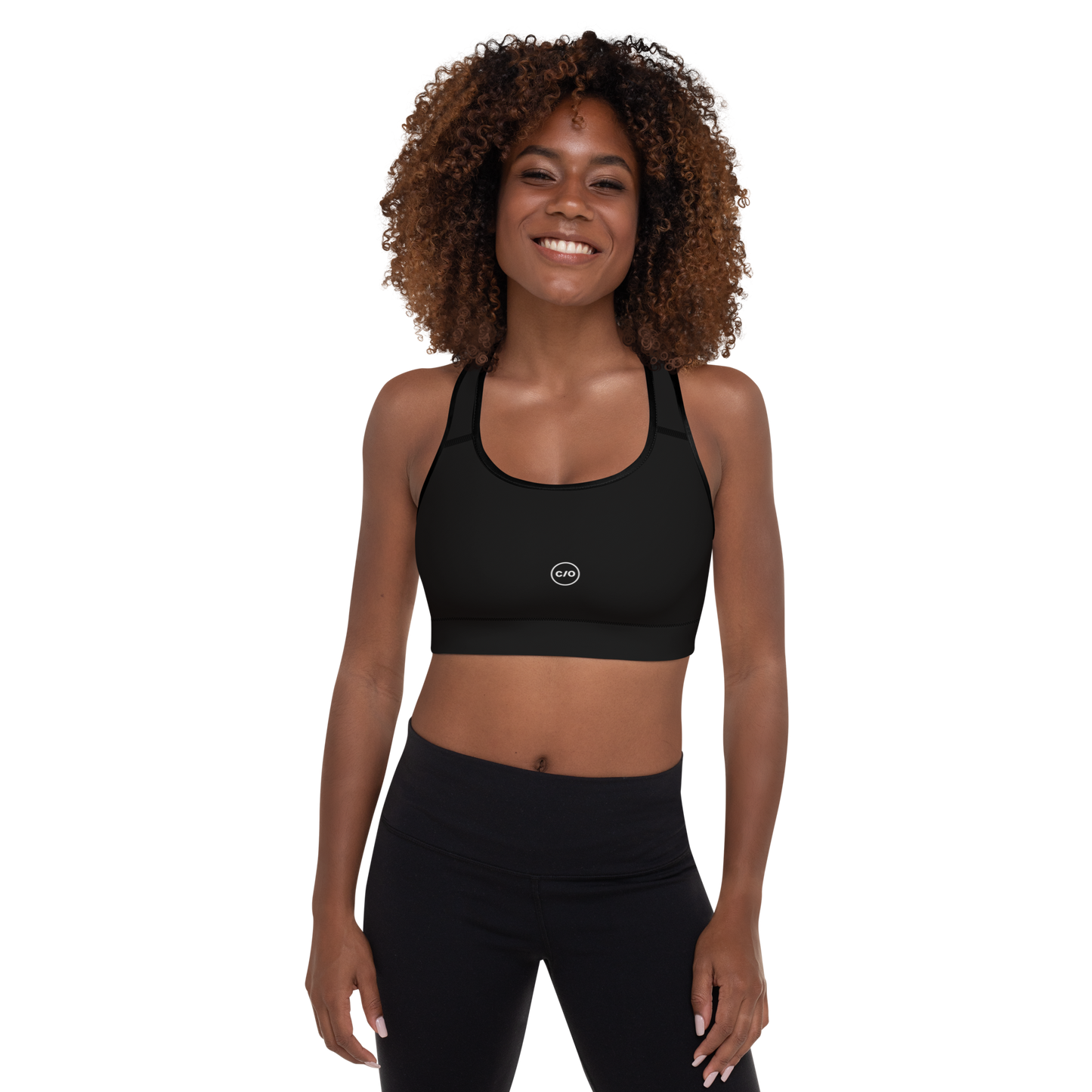 Woman wears Neue Supply Co. Essential Padded Sports Bra in Black. Front view of model smiling and looking directly into camera.