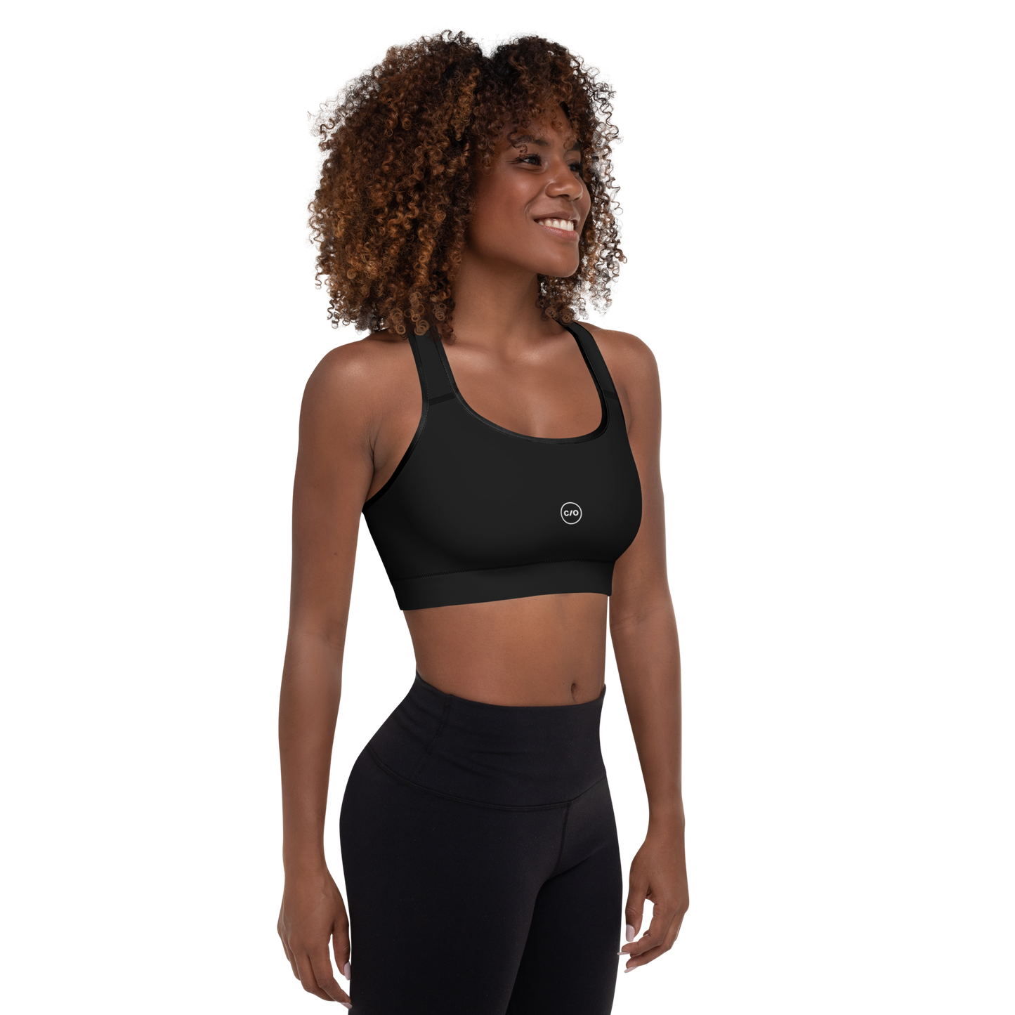 Woman wears Neue Supply Co. Essential Padded Sports Bra in Black. 3/4 view of model smiling.